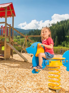 A girl playing on a playground on a spring rider shaped like a horse.