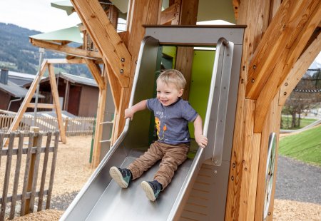 Young boy happily sliding down a metal slide on a wooden playground structure