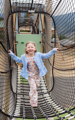 Lächelndes Mädchen klettert in einem gesicherten Netzgang auf einem Spielplatz im Freien