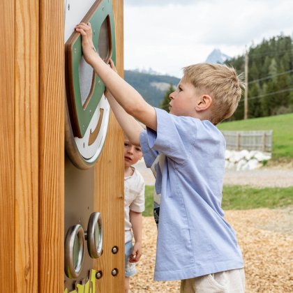 Junge spielt an einer hölzernen Spielwand im Freien mit Bergen im Hintergrund