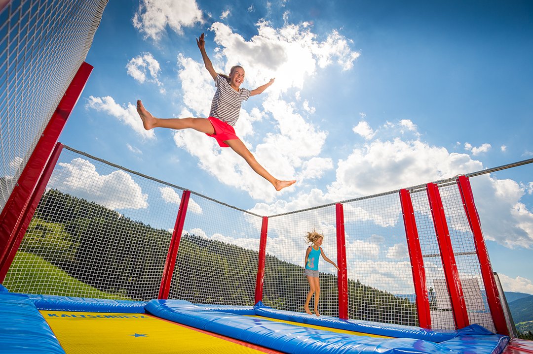 Zwei Kinder springen fröhlich auf einem Trampolin unter blauem Himmel.
