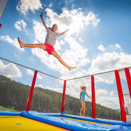 Zwei Kinder springen fröhlich auf einem Trampolin unter blauem Himmel.