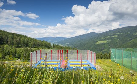 Ein Trampolinbereich mit bunten Sprungmatten inmitten einer Berglandschaft.