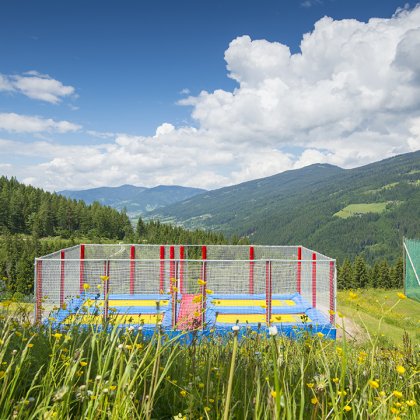 Ein Trampolinbereich mit bunten Sprungmatten inmitten einer Berglandschaft.
