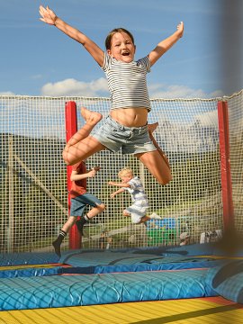 Child joyfully jumping on an outdoor trampoline with net enclosure