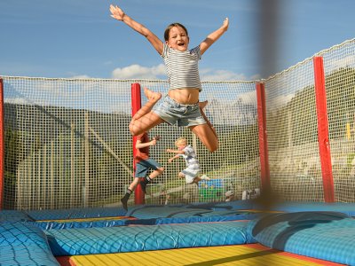 Kind springt fröhlich auf einem Trampolin mit Netzumzäunung im Freien