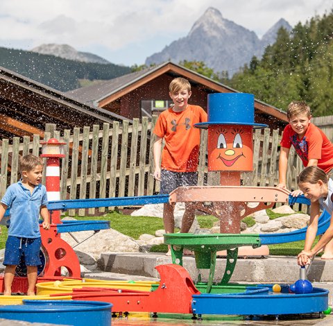 Größere Kinder spritzen mit Wasser am bunten Wasserspielplatz