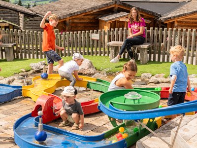 Große und kleine Kinder spielen mit der Kinderbetreuerin am Wasserspielplatz