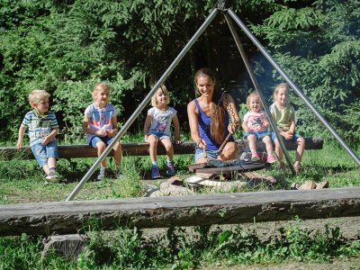 Kinder und Erwachsene sitzen rund um ein Lagerfeuer und genießen die Zeit.
