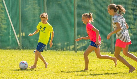 Kinder spielen Barfuß Fußball auf einem grünen Rasenplatz.