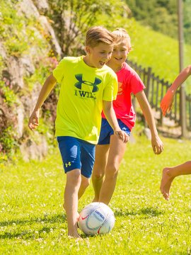 Kinder spielen gemeinsam Fußball auf einer grünen Wiese.