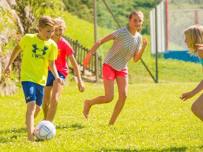 Kinder spielen gemeinsam Fußball auf einer grünen Wiese.