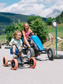 Kinder fahren Kettcars auf einer Straße und umgehen Hindernisse.