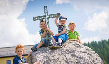 Kinder sitzen auf einem Felsen, spielen mit einer Kreuzstruktur und lächeln.