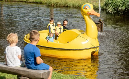 Familie fährt mit einem gelben Tretboot in Entenform auf dem Teich.