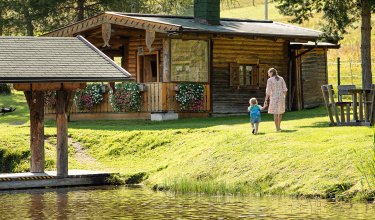 Mutter und Kind gehen Hand in Hand zu einer rustikalen Holzhütte.