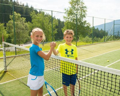 Zwei Kinder geben sich nach dem Tennisspiel die Hand am Netz.