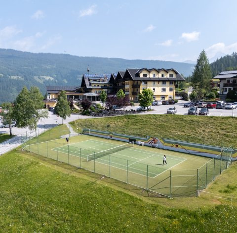 Tennisplatz mit zwei Spielern vor Hotelanlage in alpiner Landschaft