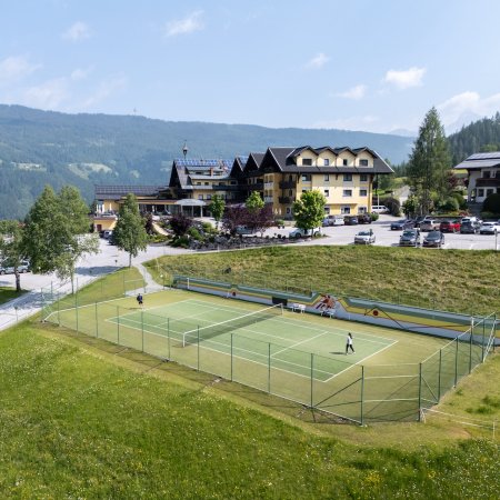 Tennisplatz mit zwei Spielern vor Hotelanlage in alpiner Landschaft