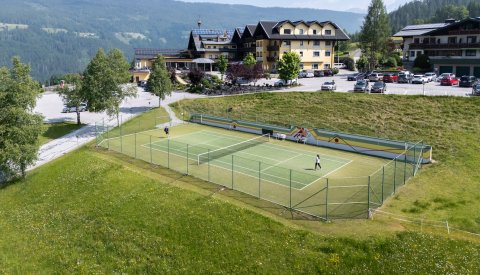 Tennisplatz mit zwei Spielern vor Hotelanlage in alpiner Landschaft