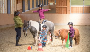 Kinder üben Voltigieren und Ponyführen in der Reithalle.