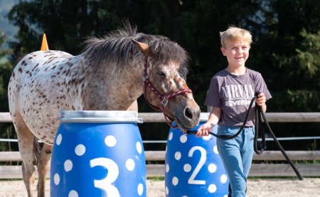 Junge führt Pony an der Leine neben blauen Fässern mit den Zahlen 2 und 3