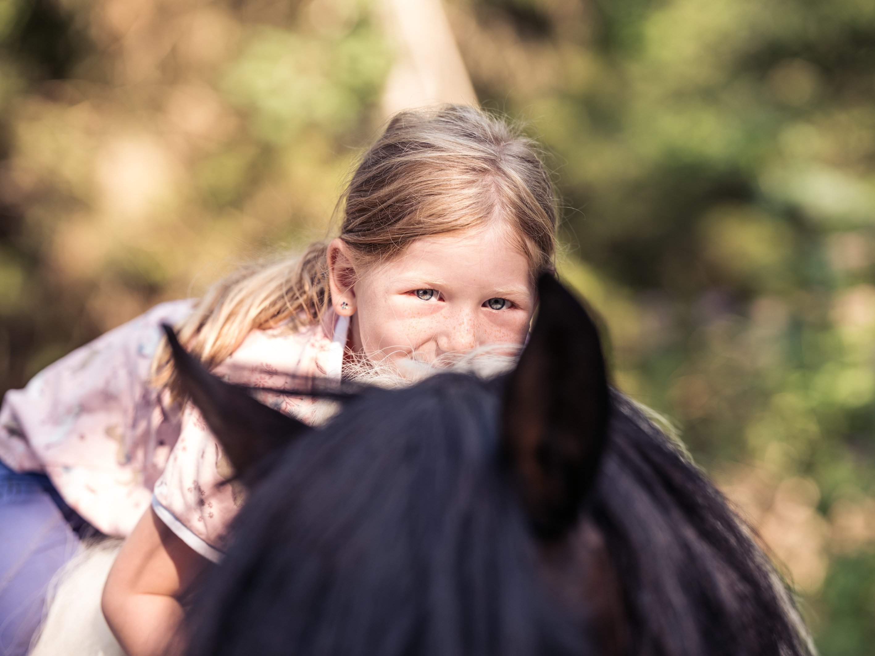 Mädchen mit blonden Haaren liegt auf einem Pferd, Blick über das Pferdehaupt