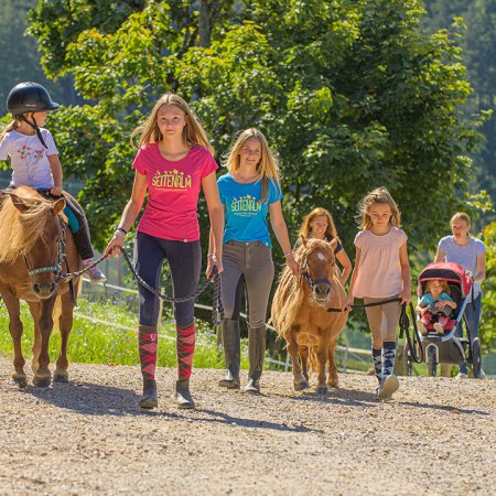 Kinder reiten und führen Ponys auf einem sonnigen Schotterweg.