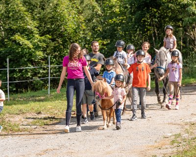 Kinder und Erwachsene führen gemeinsam Ponys auf einem sonnigen Waldweg.