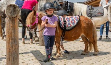 Ein Mädchen mit Reithelm steht neben einem braunen Pony.