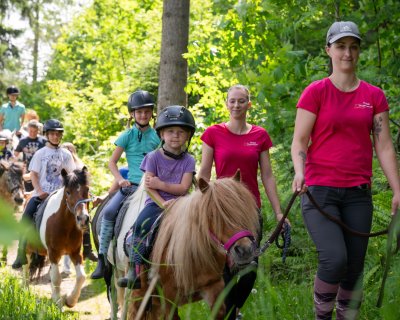 Mädchen reitet auf einem Pony, begleitet von zwei Betreuerinnen.
