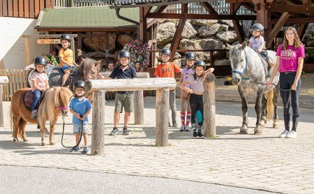 Kindergruppe mit Ponys beim Reitplatz, begleitet von einer Betreuerin.