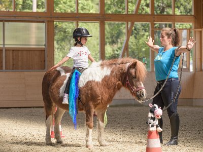 Kind übt Voltigierübung auf Pony unter Anleitung in der Reithalle.