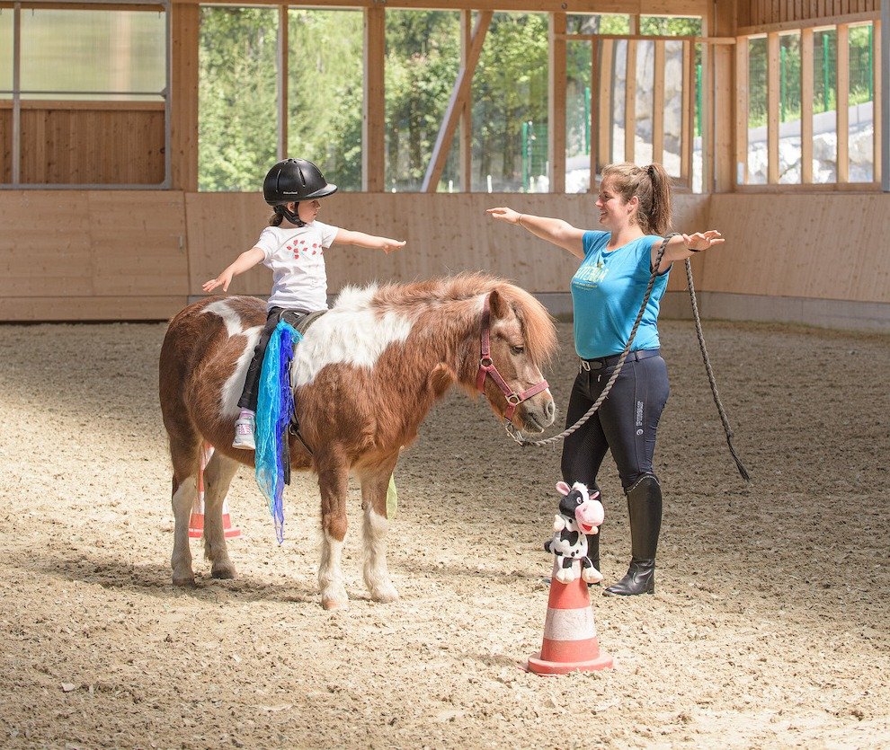 Kind übt Voltigierübung auf Pony unter Anleitung in der Reithalle.