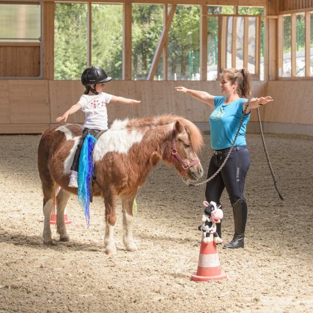 Kind übt Voltigierübung auf Pony unter Anleitung in der Reithalle.