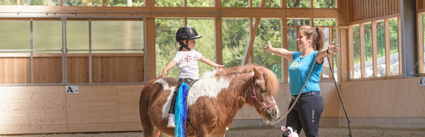 Kind auf Pony beim Reitunterricht mit der Reitlehrerin