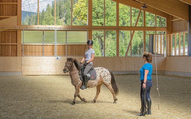 Kind beim Reitunterricht in der Reithalle