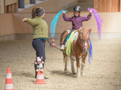 Kind balanciert fröhlich mit bunten Tüchern auf einem Pony beim Voltigieren.