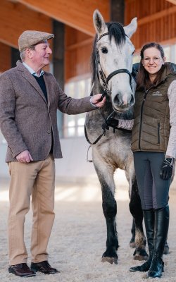 Mann und Frau stehen mit einem Pferd in einer Reithalle, der Mann hält die Zügel