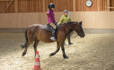 Mädchen balanciert auf einem Pony beim Voltigieren in der Reithalle.