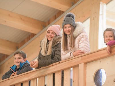 Lächelnde Kinder lehnen sich über ein Holzgeländer in der Reithalle.