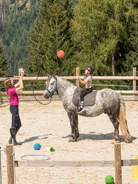 Mädchen auf Pferd wirft Ball auf hängendes Ziel.