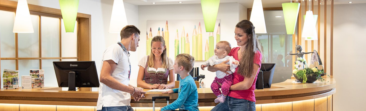 Familie checkt mit Gepäck an der Rezeption herzlich ein.