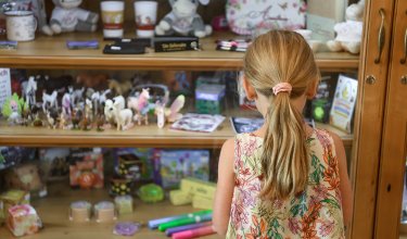 Child with ponytail and floral dress looking at a display case filled with toys and souvenirs
