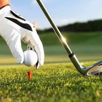 Behandschuhte Hand platziert Golfball auf Tee neben Eisen-Schläger im Gras.