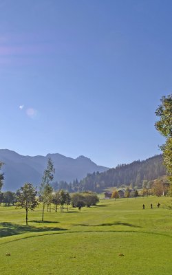 Golfplatz mit viel Grün und Bergpanorama an einem klaren Morgen.