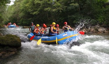 Gruppe erlebt Wildwasser-Rafting-Abenteuer auf einem Fluss im Wald.