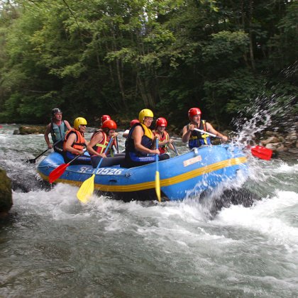 Gruppe erlebt Wildwasser-Rafting-Abenteuer auf einem Fluss im Wald.