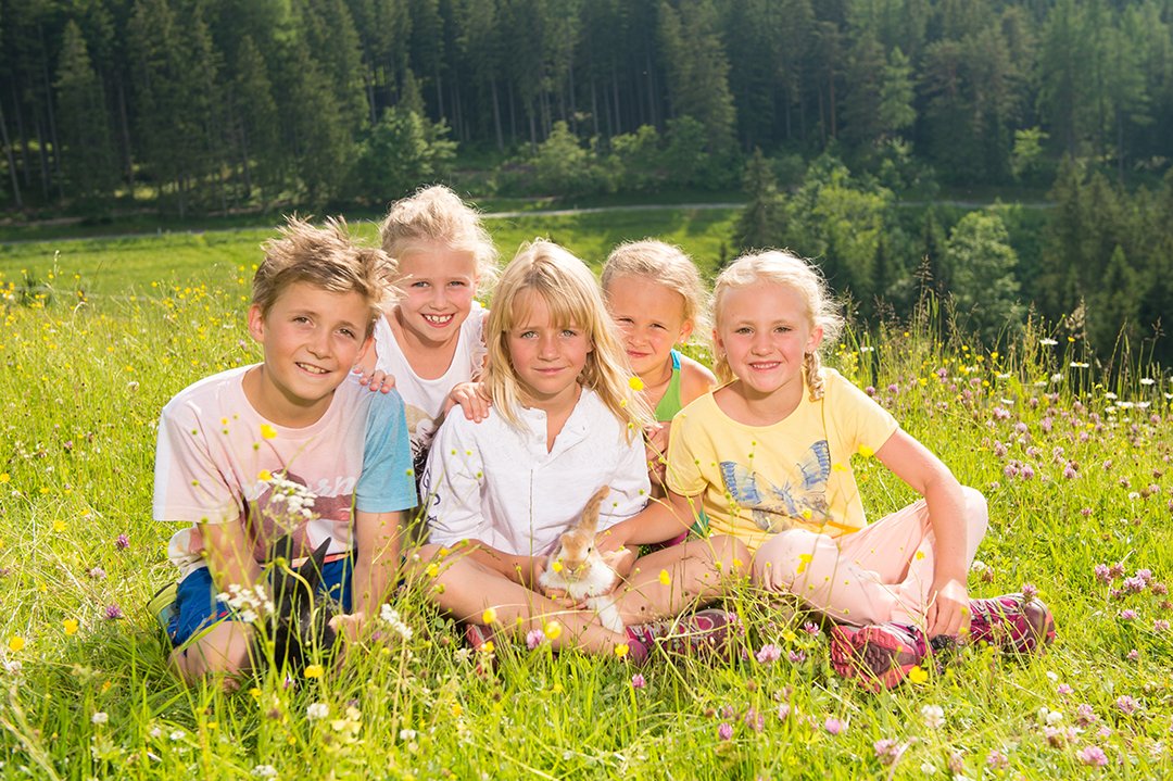 Kinder sitzen in Blumenwiese und kuscheln ein Kaninchen in der Sonne.
