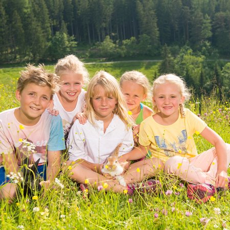 Kinder sitzen in Blumenwiese und kuscheln ein Kaninchen in der Sonne.